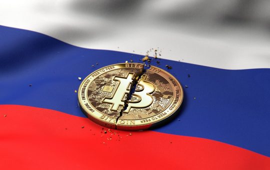 A cracked token representing Bitcoin rests on a Russian flag.